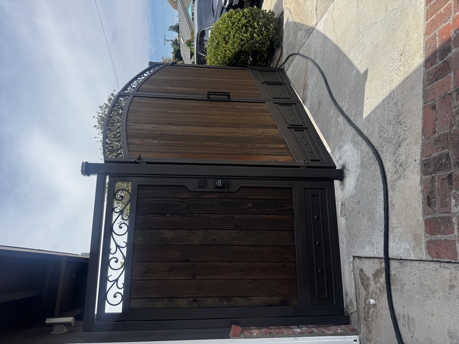 Custom wood and iron arched driveway gate with ornamental scrollwork and a matching pedestrian gate