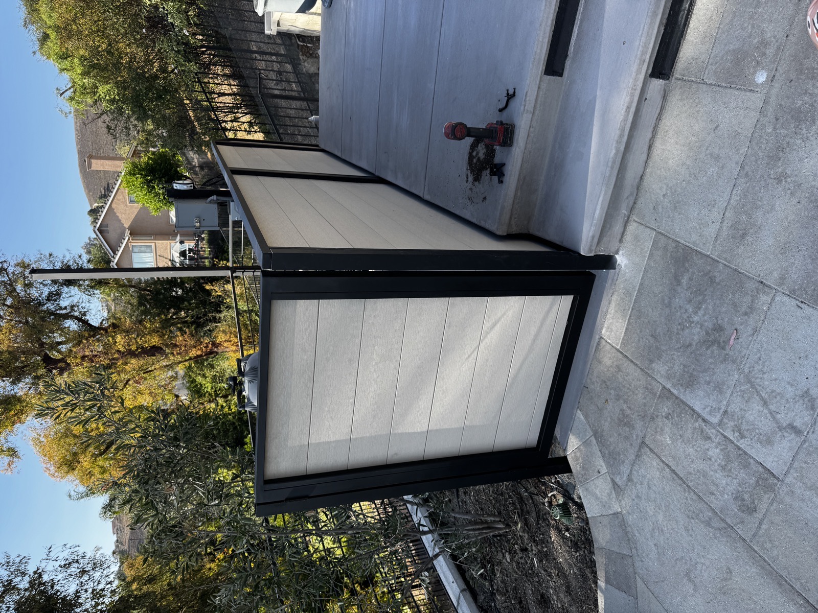 Modern privacy screen with a black steel frame and light composite horizontal panels on a hillside patio
