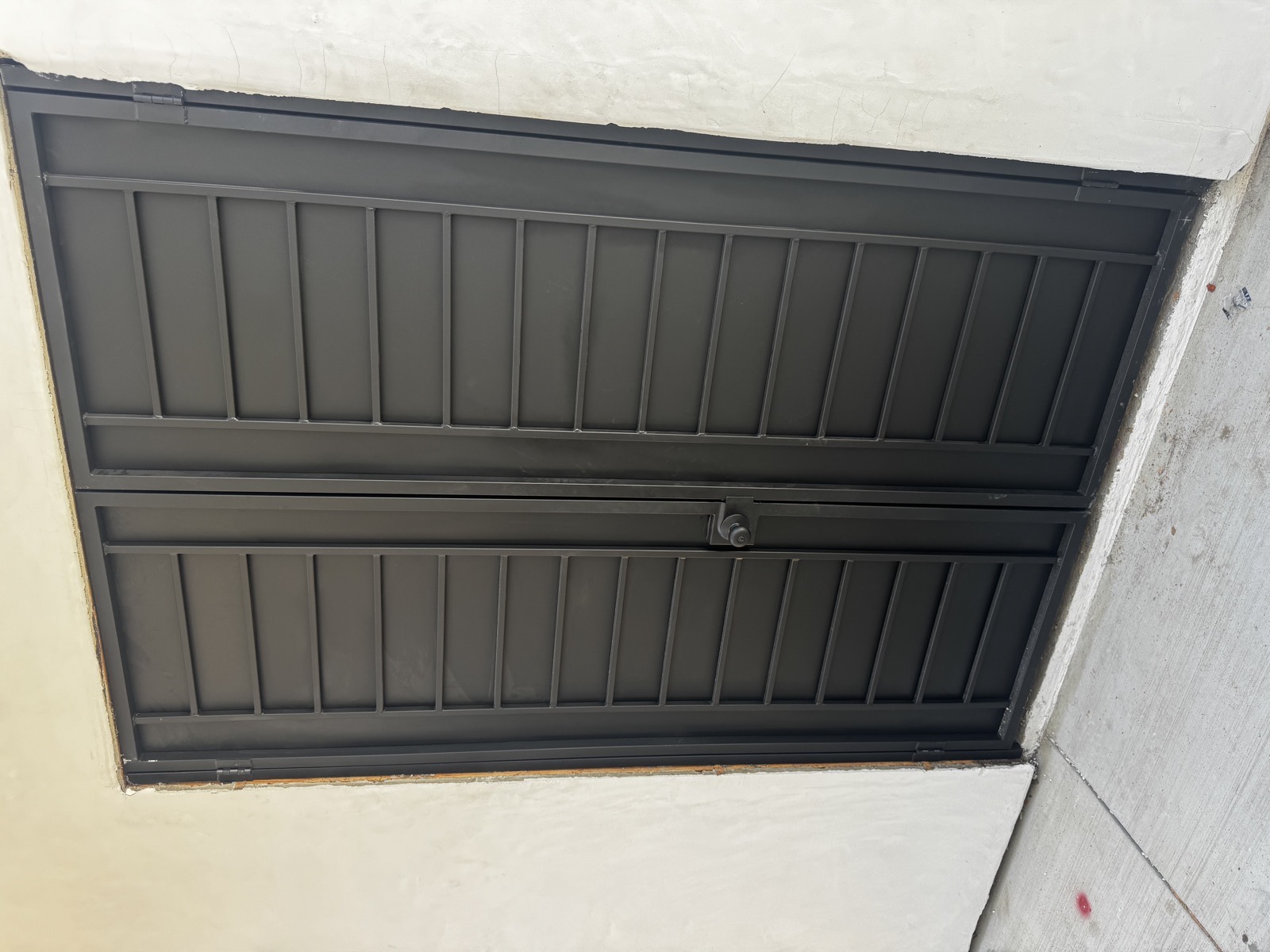Black double metal doors with horizontal panel detailing set into a stucco opening